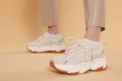 Photo of Woman wearing pair of new stylish sneakers on beige background, closeup