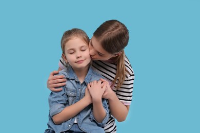 Photo of Young woman kissing her little daughter on light blue background. Happy Mother's Day