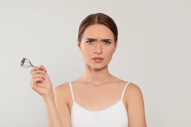 Emotional woman with eyelash curler on white background, space for text