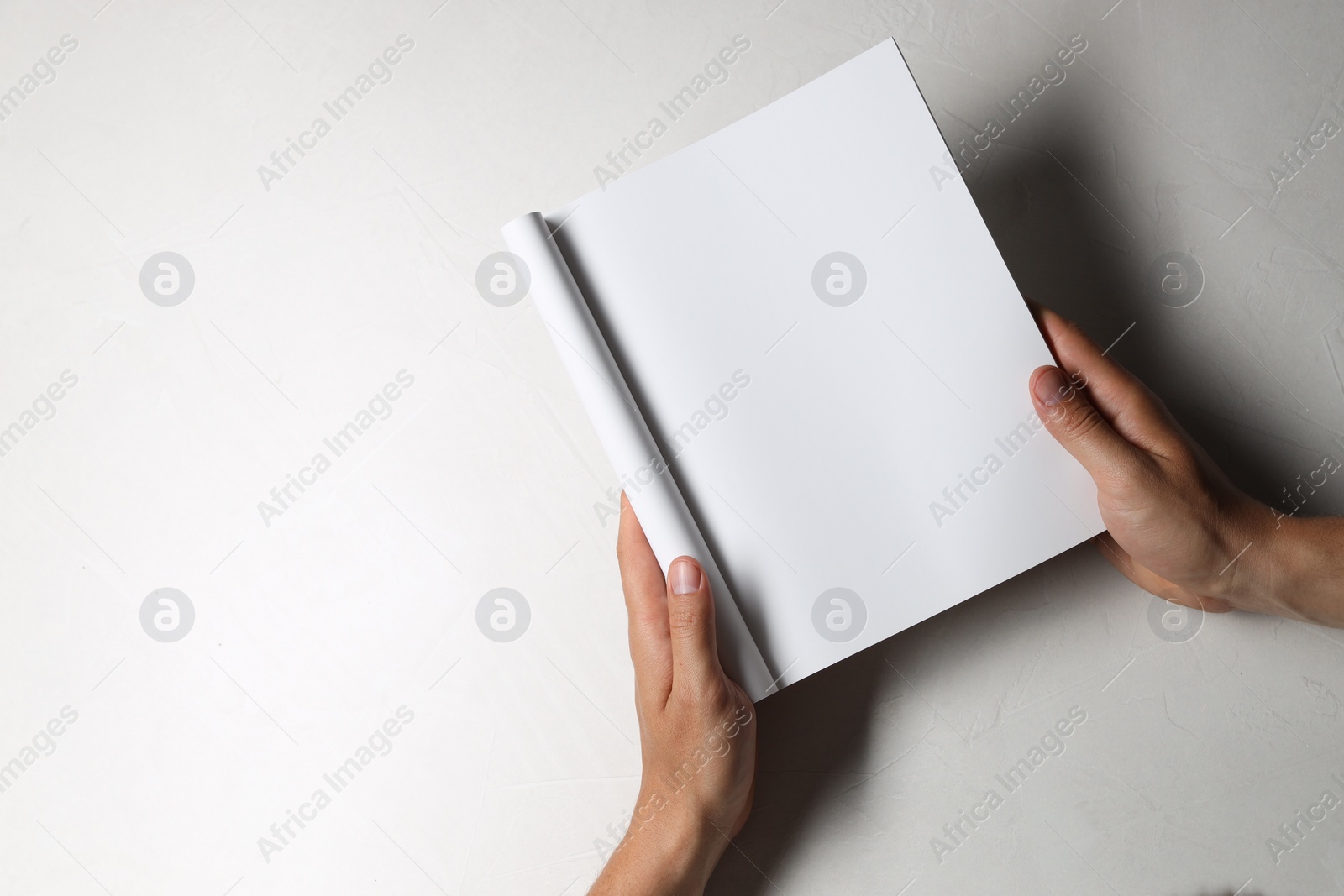 Photo of Man holding blank notebook at white table, top view. Mockup for design