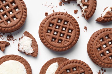 Tasty chocolate sandwich cookies with cream on white background, flat lay