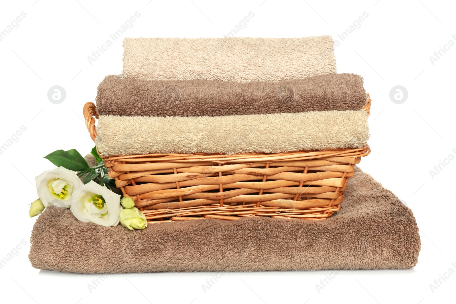 Photo of Wicker basket with folded soft terry towels and flowers on white background