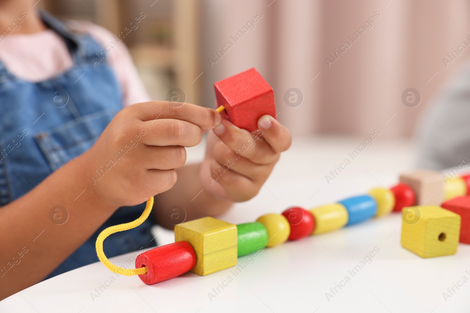 Photo of Motor skills development. Little girl playing with wooden pieces and string for threading activity at table indoors, closeup