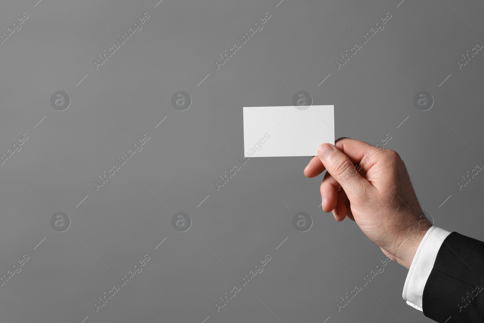 Photo of Man holding blank business card on grey background, closeup. Space for text