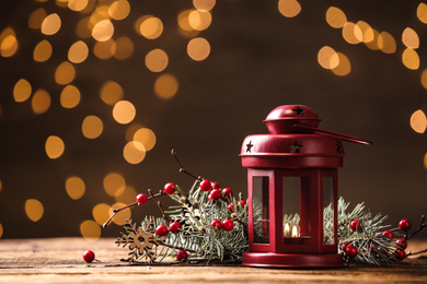 Photo of Lantern and Christmas decor on wooden table against blurred festive lights, space for text. Winter holiday