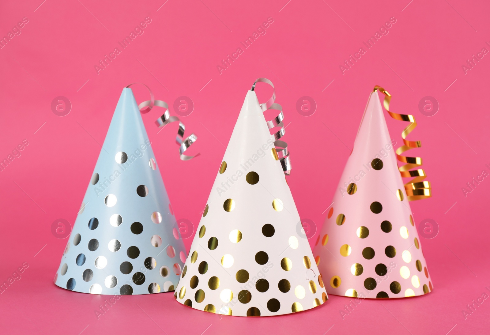 Photo of Bright party hats with streamers on pink background