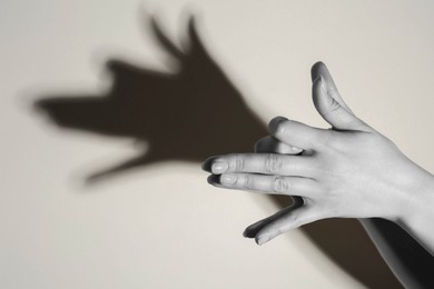 Photo of Shadow puppet. Woman making hand gesture like dog on light background, closeup. Black and white effect