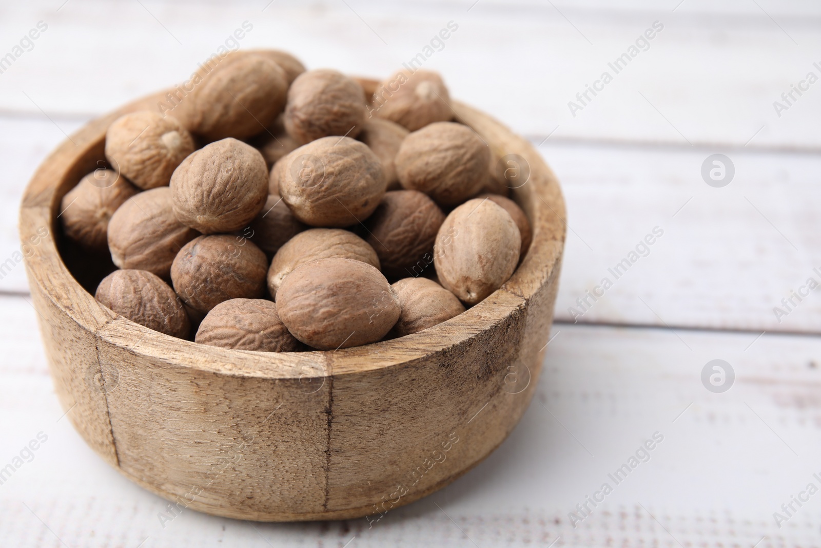 Photo of Whole nutmegs in bowl on light wooden table, closeup. Space for text