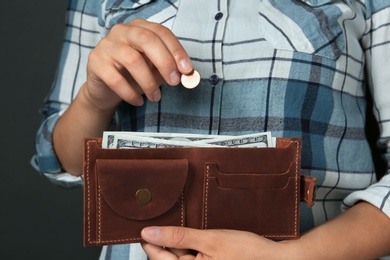 Young woman putting coin into wallet on grey background, closeup