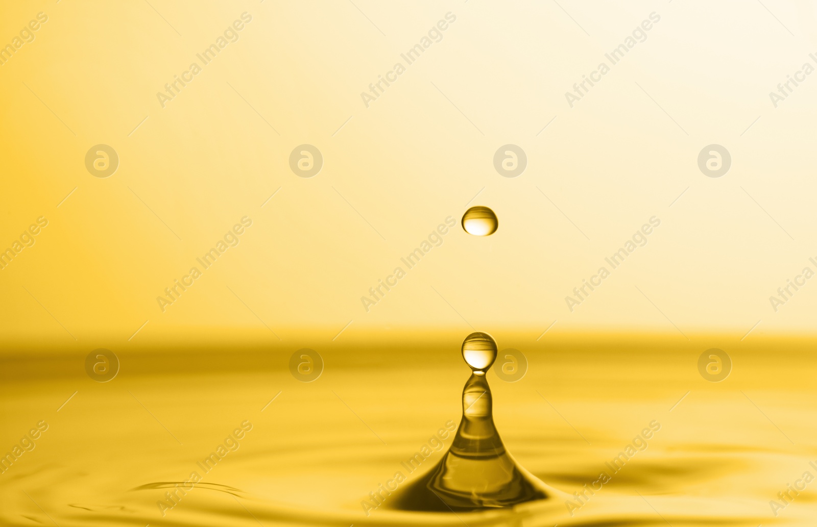 Image of Splash of golden oily liquid with drop on yellow background, closeup. Space for text