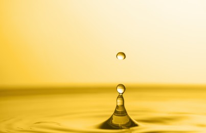 Image of Splash of golden oily liquid with drop on yellow background, closeup. Space for text