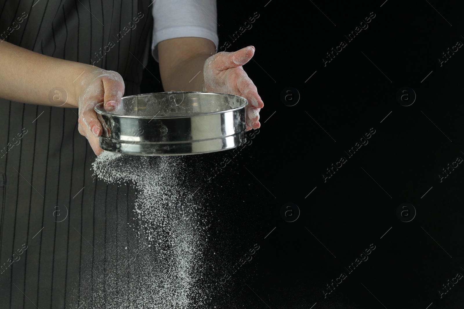 Photo of Woman sieving flour at table against black background, closeup. Space for text