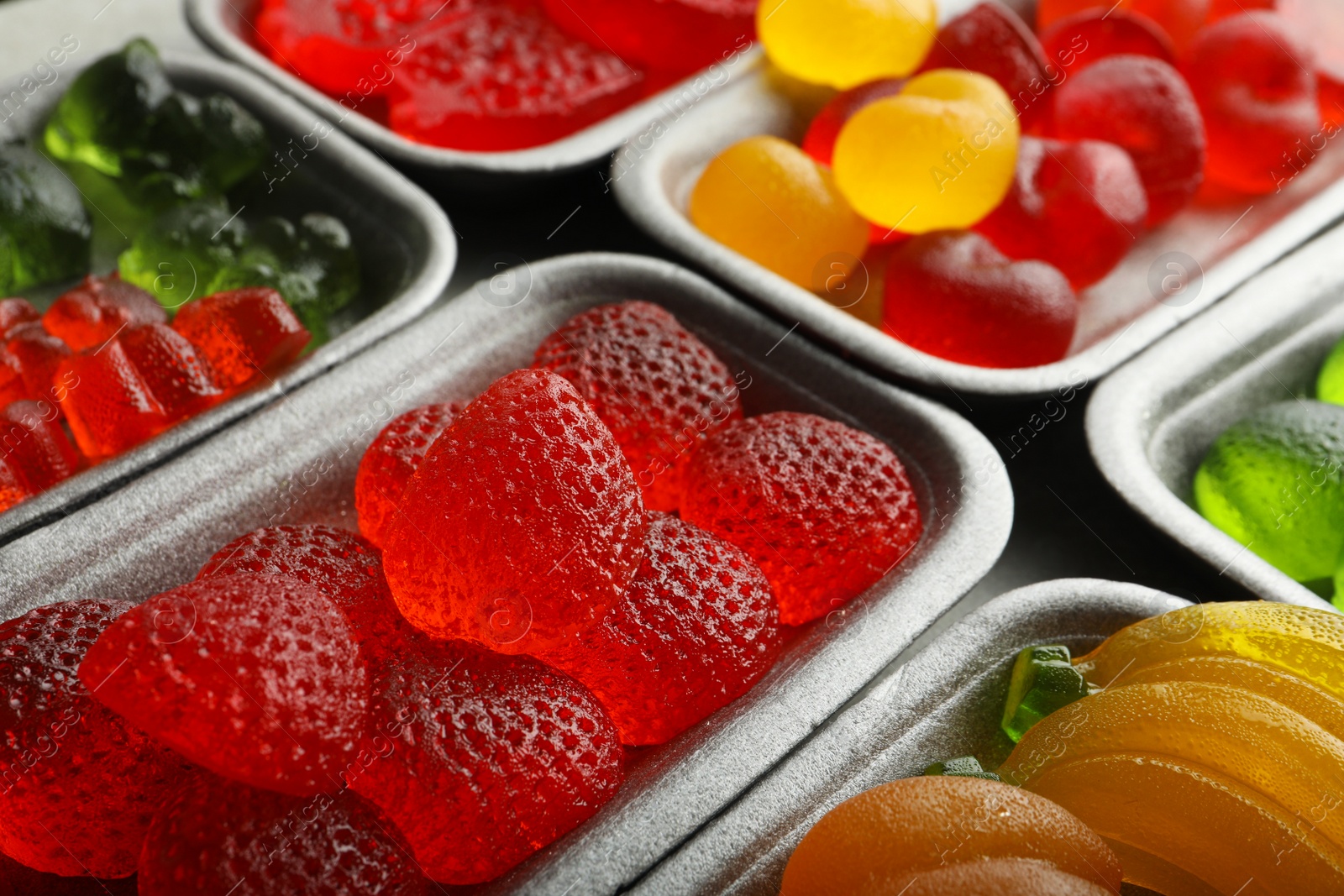 Photo of Different delicious gummy candies in containers, closeup