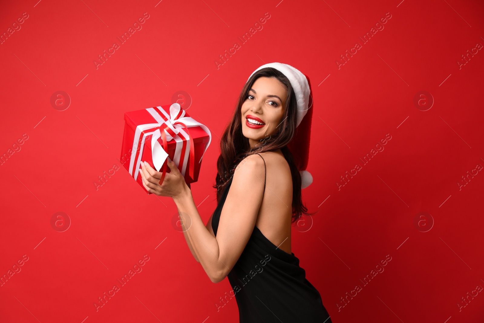 Photo of Beautiful woman wearing Santa hat with Christmas gift on red background