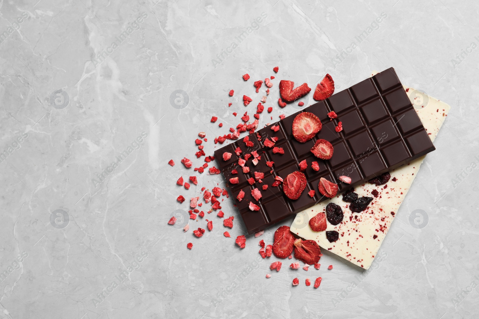 Photo of Different chocolate bars with freeze dried fruits on light marble table, top view. Space for text