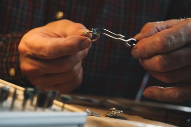Professional jeweler working with ring at wooden table, closeup