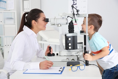 Photo of Children's doctor examining little boy with ophthalmic equipment in clinic