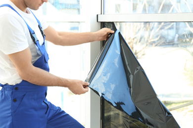 Professional worker tinting window with foil indoors, closeup
