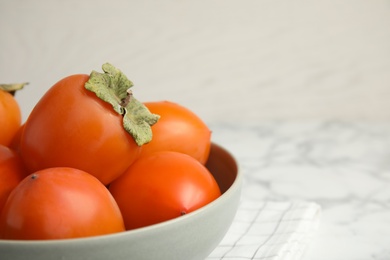 Photo of Tasty ripe persimmons in bowl on table, closeup. Space for text