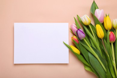 Beautiful tulips and blank card on pale pink background, flat lay