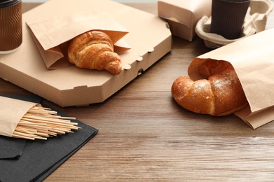 Paper bags with pastry and takeaway food on wooden table