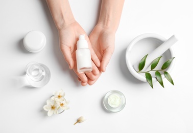 Photo of Woman holding bottle of cream over table with cosmetic products