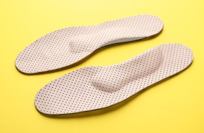 Photo of Beige orthopedic insoles on yellow background, closeup