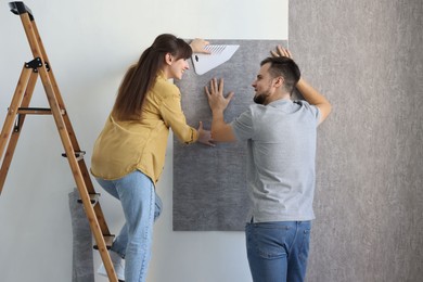 Photo of Couple hanging stylish gray wallpaper in room