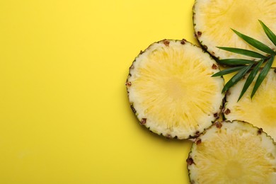 Photo of Slices of tasty ripe pineapple and green leaves on yellow background, flat lay. Space for text