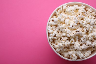 Photo of Paper bucket with delicious popcorn on pink background, top view. Space for text