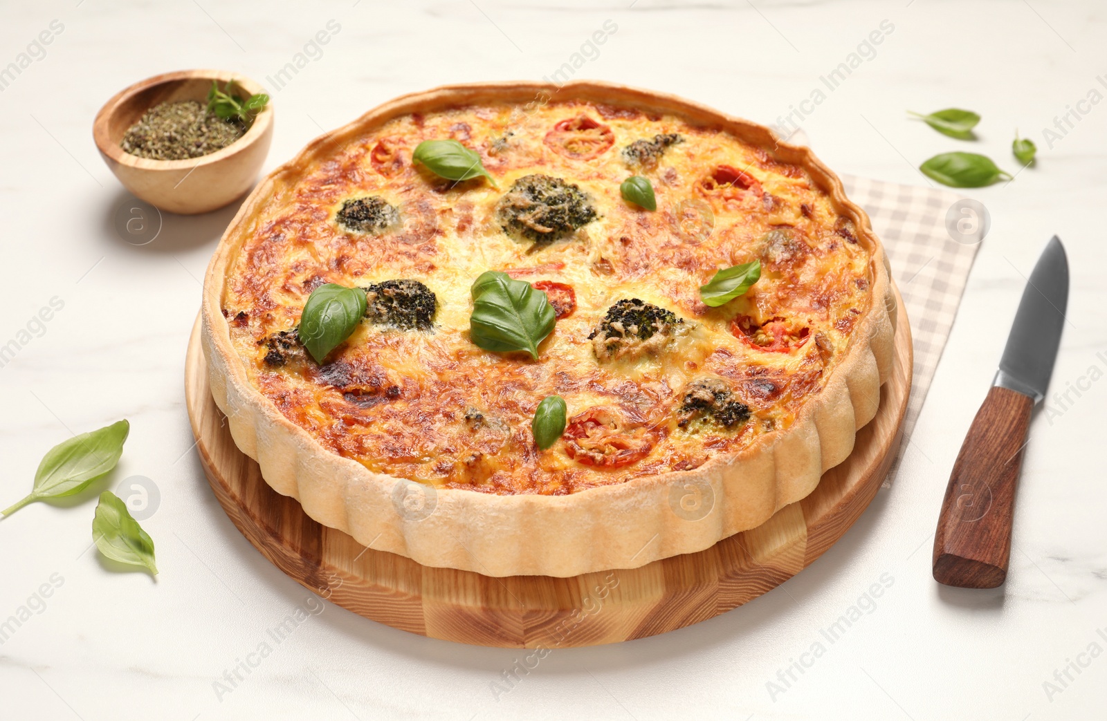 Photo of Delicious homemade vegetable quiche, basil leaves and knife on white table