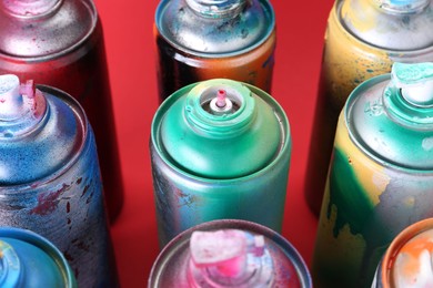 Photo of Many spray paint cans on red background, closeup