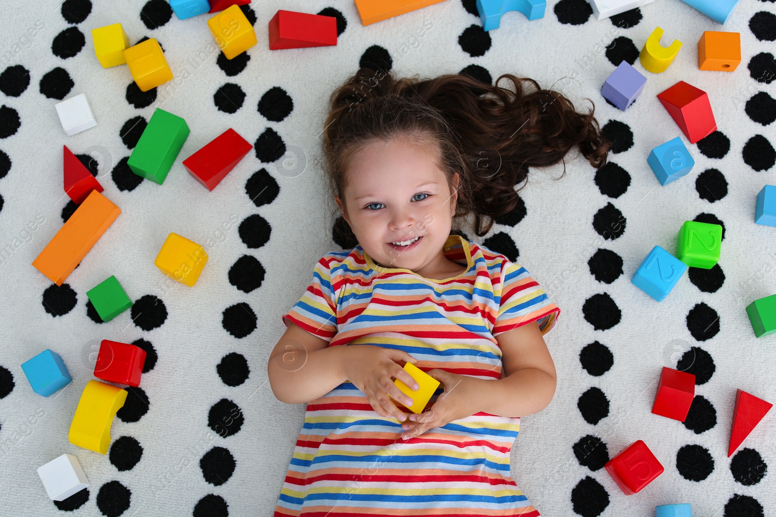 Photo of Cute little girl and toys on floor, top view