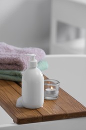 Photo of Bottle of bubble bath with foam, towels and candle on tub in bathroom