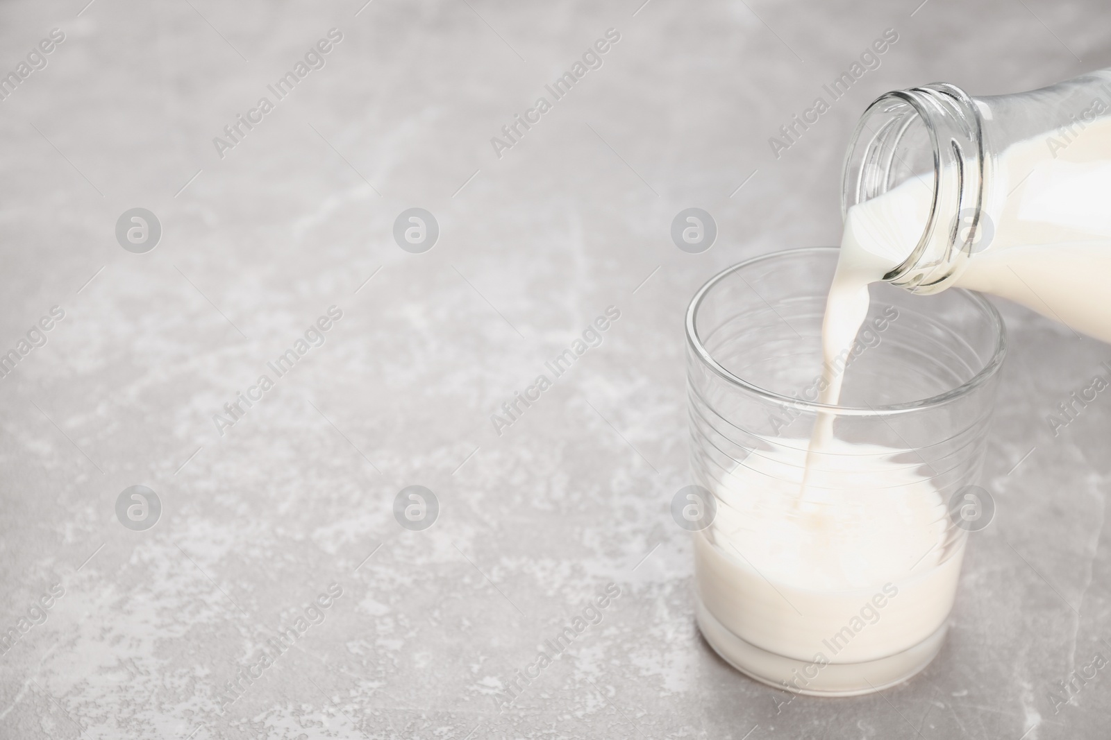 Photo of Pouring of milk from bottle into glass on table. Fresh dairy product