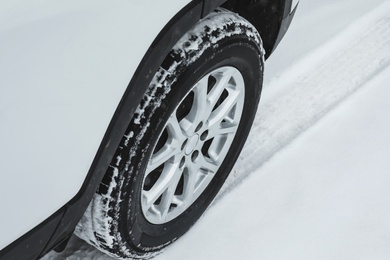 Modern car leaving tire track on snowy road, closeup view