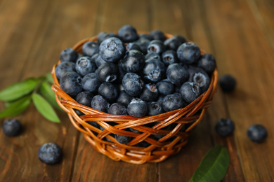 Photo of Tasty ripe blueberries in wicker bowl on wooden table