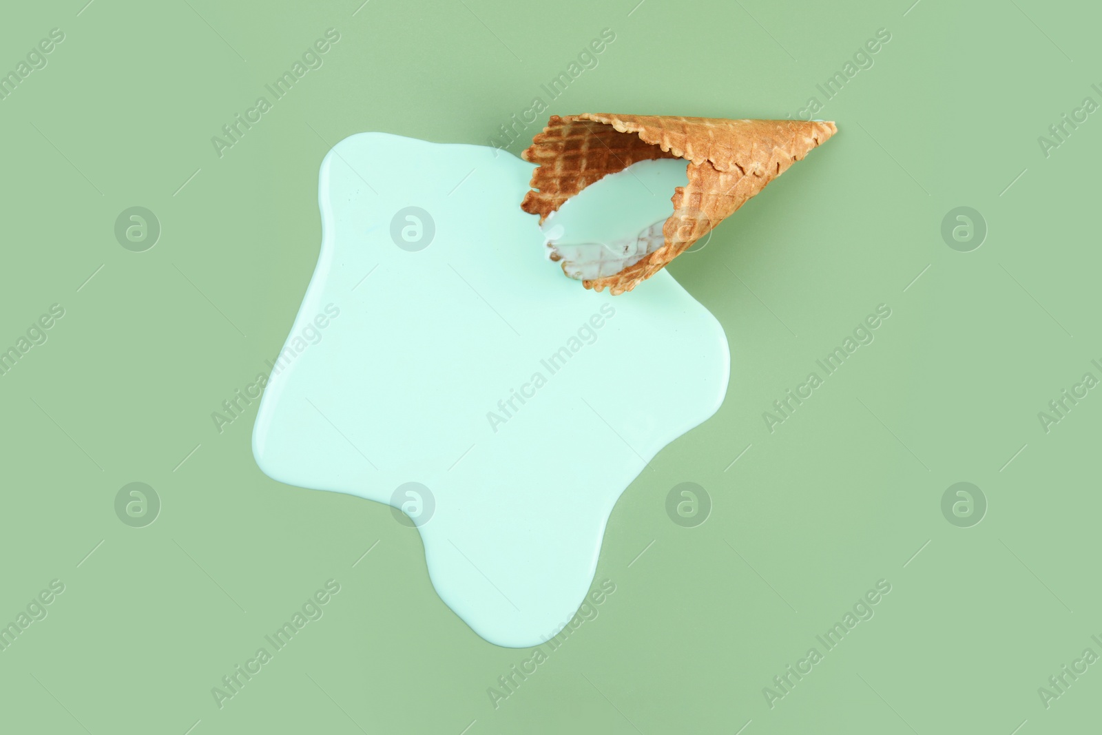 Photo of Melted ice cream and wafer cone on green background, top view