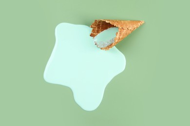 Photo of Melted ice cream and wafer cone on green background, top view