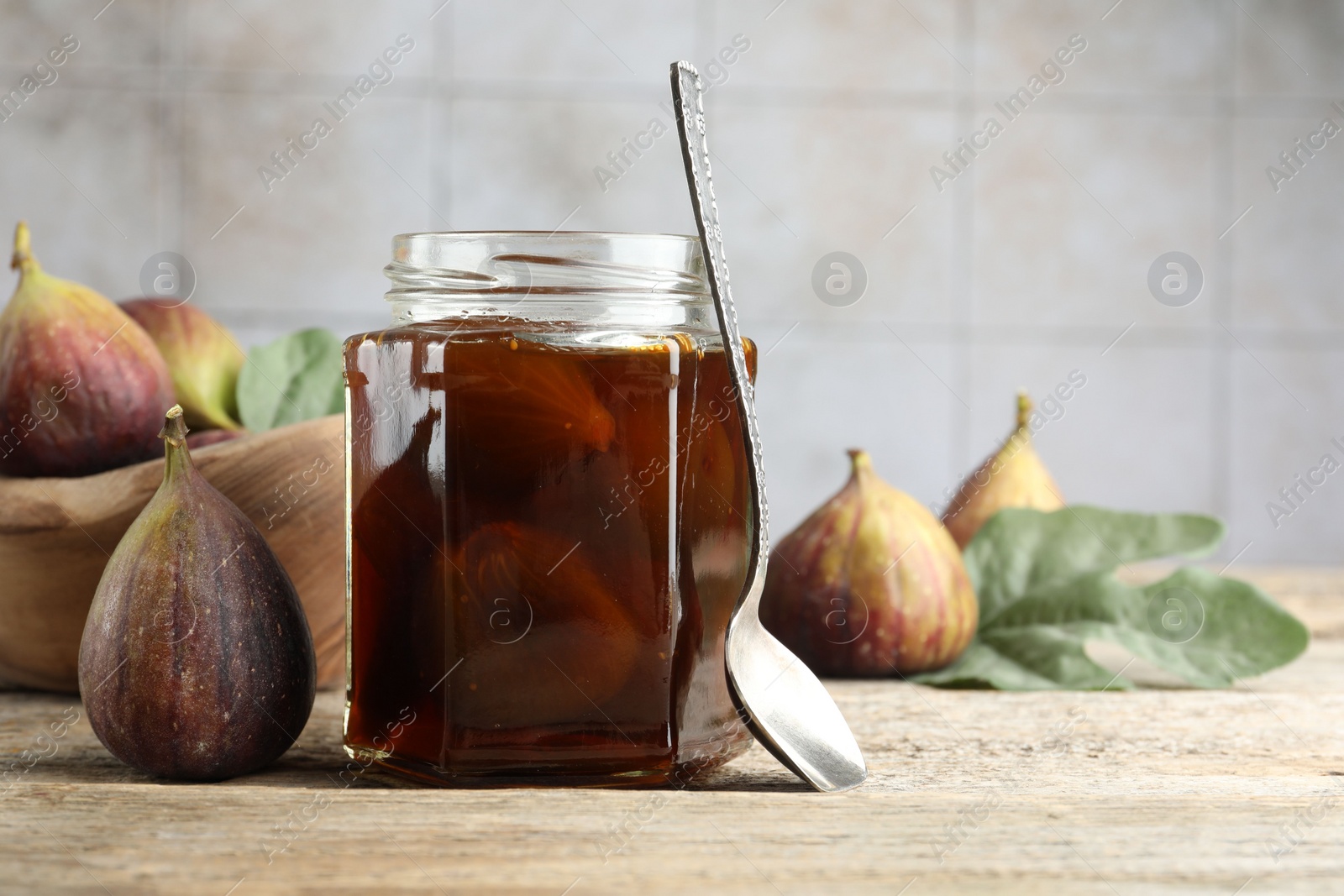 Photo of Jar of tasty sweet jam and fresh figs on wooden table. Space for text