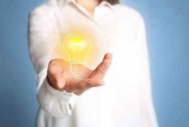 Image of Idea concept. Businesswoman demonstrating glowing light bulb illustration on light blue background, closeup