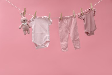 Photo of Different baby clothes and bunny toy drying on laundry line against pink background
