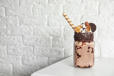 Photo of Mason jar of tasty milk shake with sweets on table near brick wall. Space for text