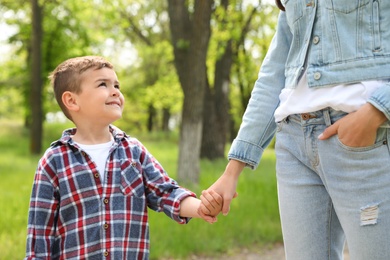 Photo of Cute little child holding hands with his mother outdoors. Family weekend