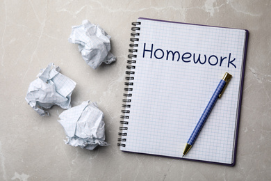 Image of Notebook with inscription HOMEWORK and crumpled paper balls on grey marble table, flat lay