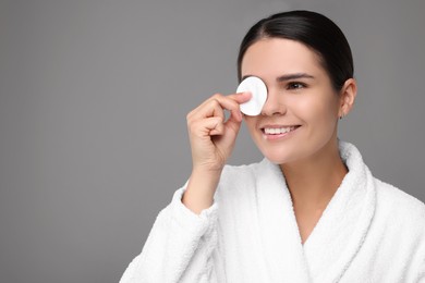 Young woman cleaning her face with cotton pad on grey background. Space for text