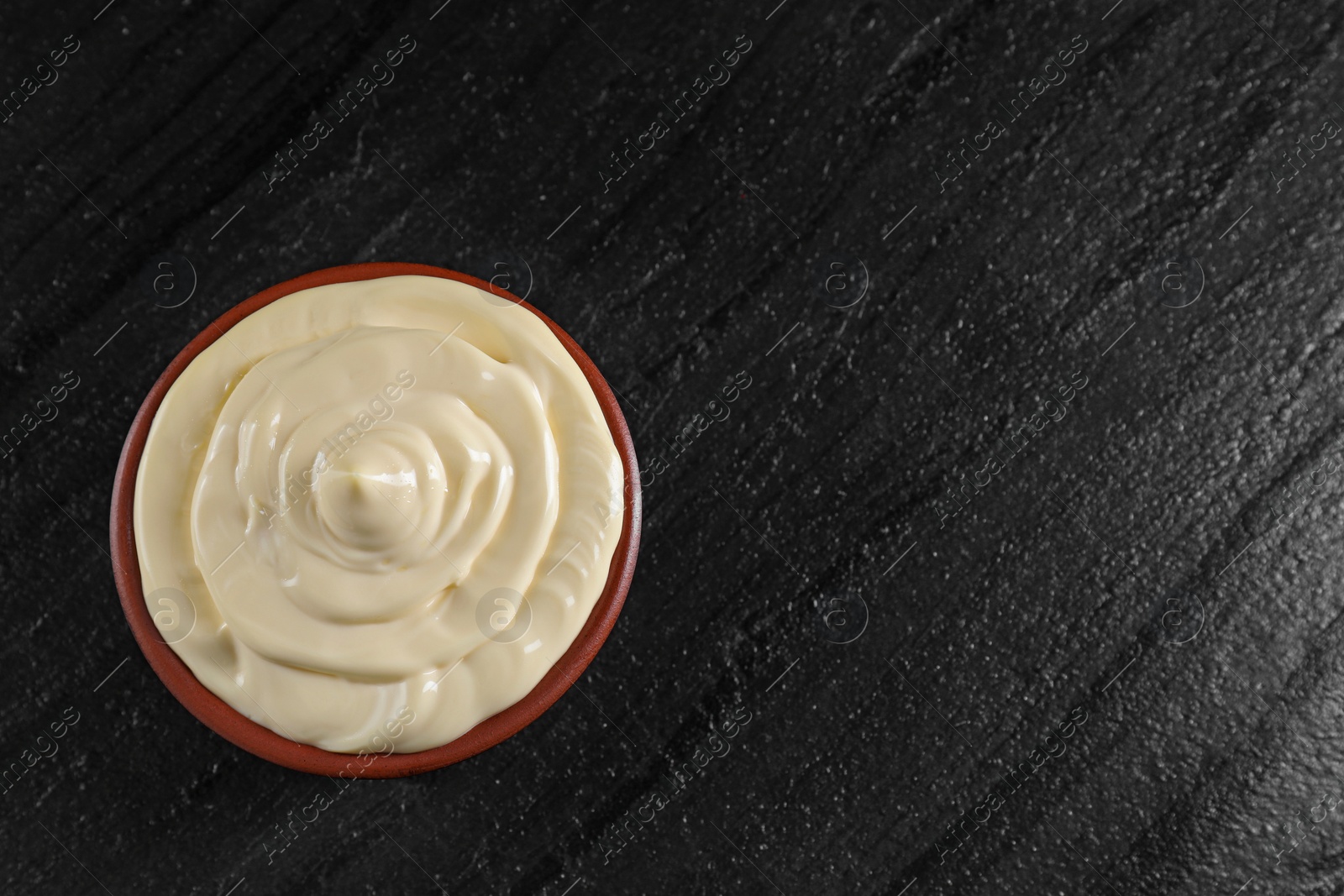 Photo of Fresh mayonnaise sauce in bowl on black table, top view. Space for text