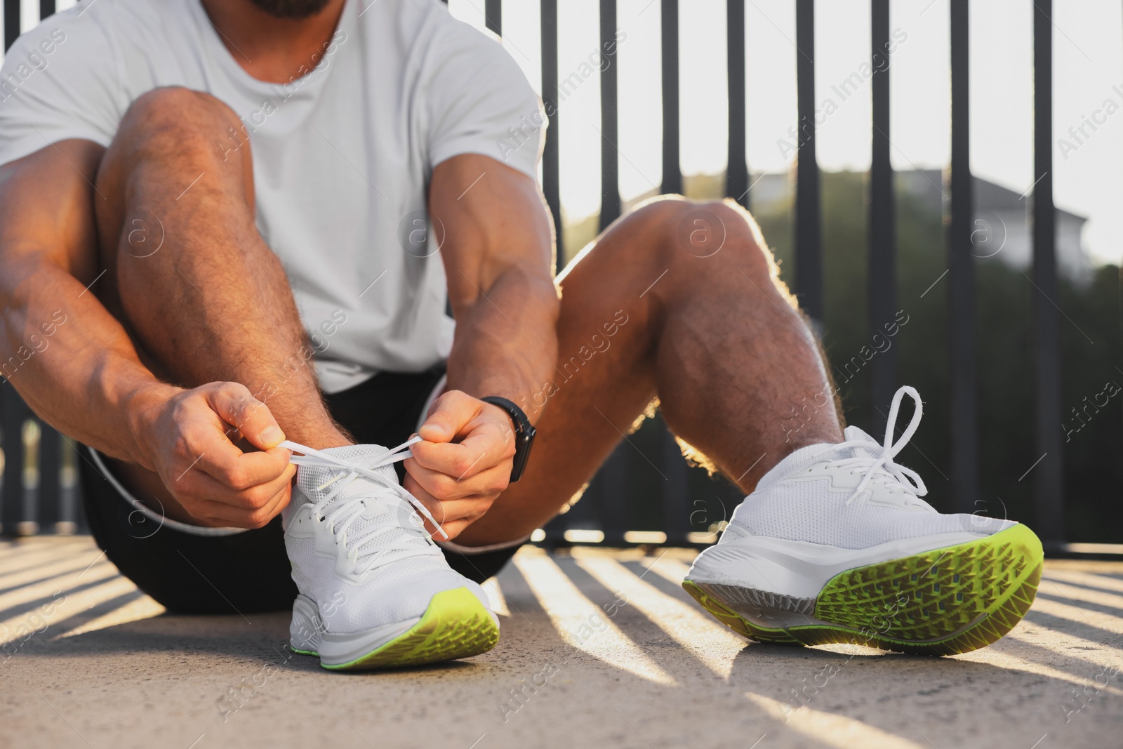 Photo of Man tying shoelaces before running outdoors on sunny day, closeup