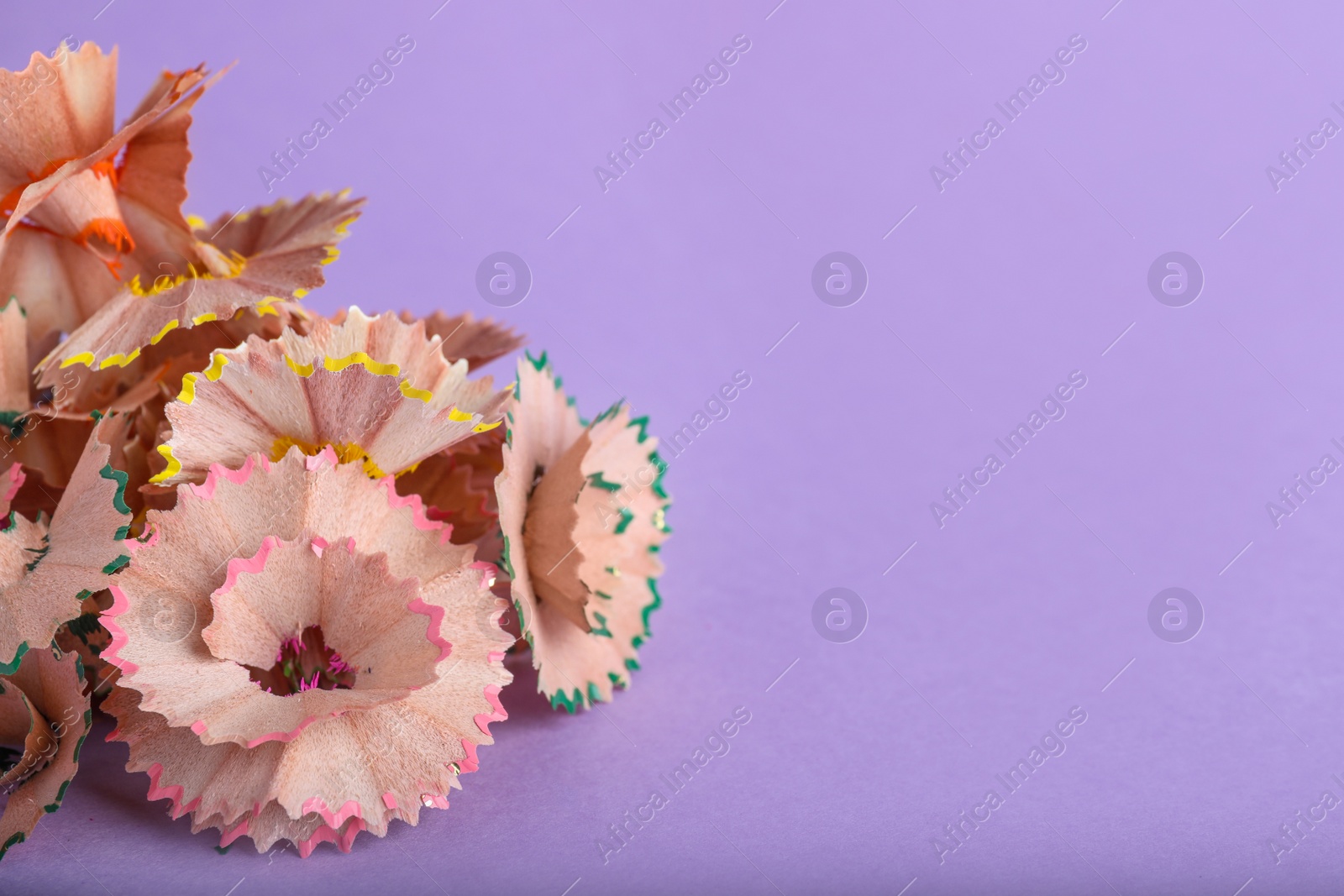 Photo of Pile of colorful pencil shavings on violet background, closeup. Space for text