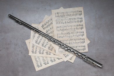 Photo of Sheets with musical notes and flute on grey table, flat lay